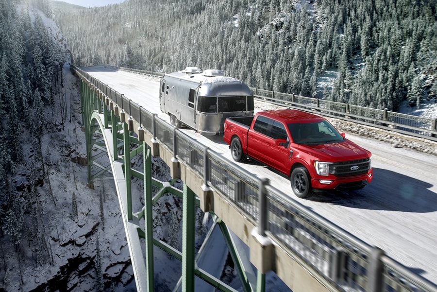 Image of a 2023 Ford F-150® XLT in Rapid red pulling an airstream camper over a suspension bridge