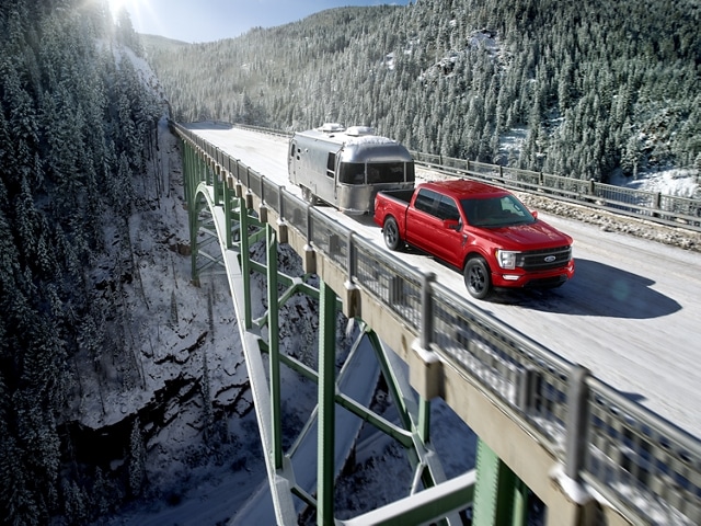 Image of a 2023 Ford F-150® XLT in Rapid red pulling an airstream camper over a suspension bridge