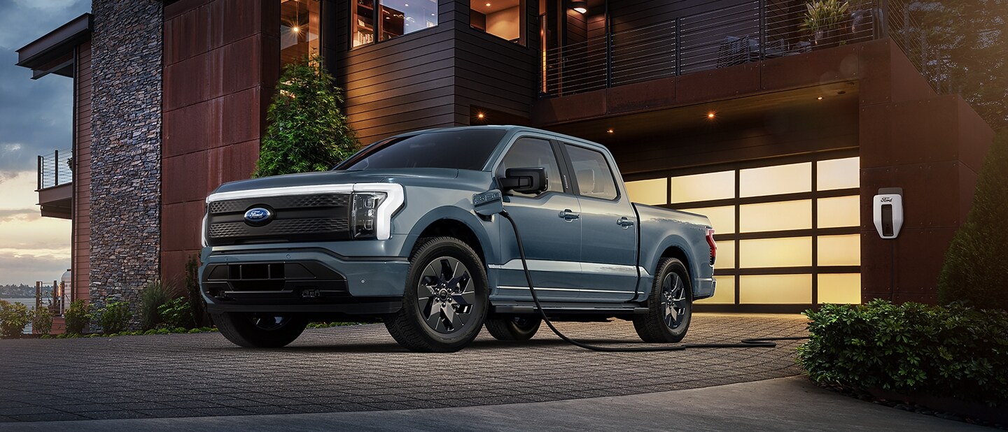 2023 Ford F-150® Lightning in Azure Gray parked in front of a home hooked up to a home charger