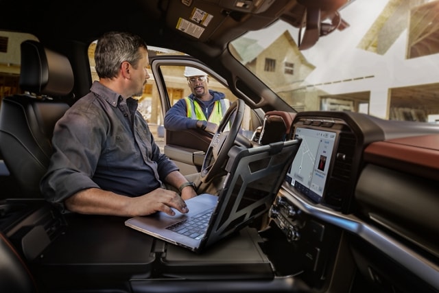 Dos hombres hablando mientras uno trabaja en una laptop en la cabina de la camioneta