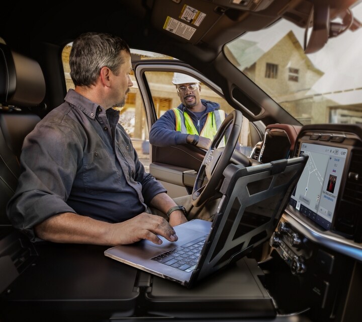 Un hombre utilizando una computadora portátil en la superficie de trabajo interior mientras habla con un compañero de trabajo
