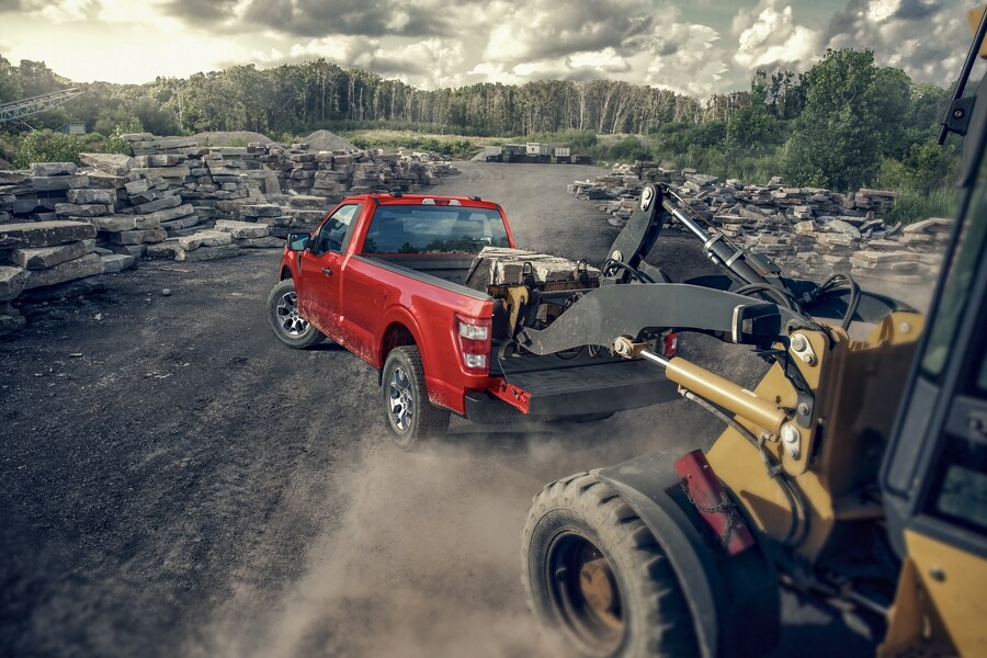 A tractor loading construction materials into the rear tailgate area of a 2023 Ford F-150® at a work site