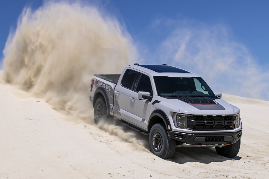 A 2023 Ford F-150® FX4 in Rapid Red Metallic Tinted Clearcoat being driven down a sloped dirt road kicking up dust