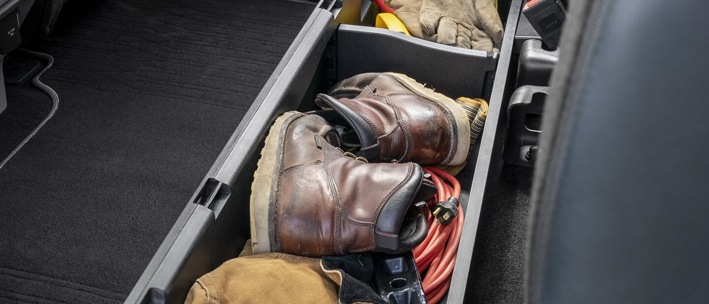 Interior de una Ford F-150® 2023 que muestra el almacenamiento plegable dividido abierto con equipos en el interior, disponible debajo del asiento trasero