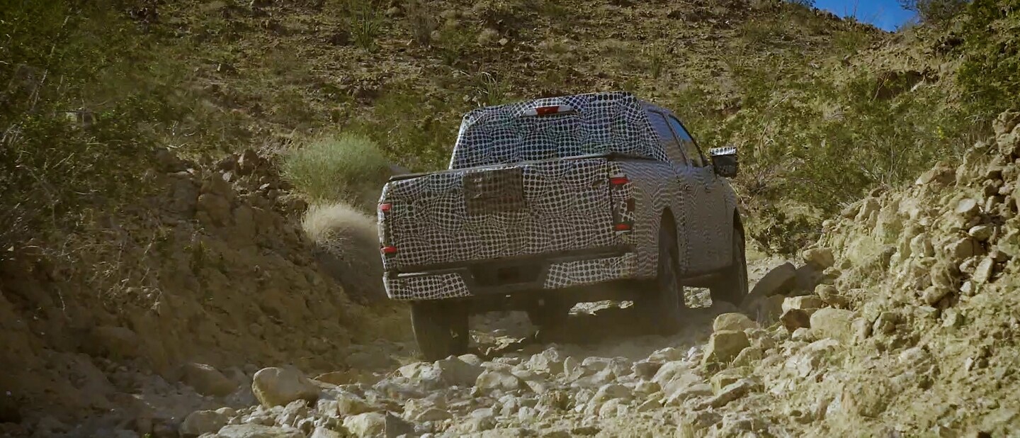 Rear shot of a 2023 Ford F-150® covered in disguise wrap off-roading through a desert gully