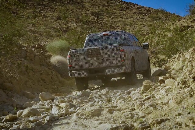 Rear shot of a 2023 Ford F-150® covered in disguise wrap off-roading through a desert gully