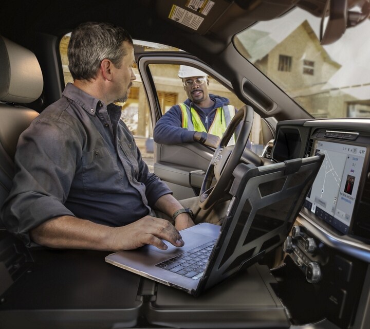 Person using the center console of Interior Work Surface to work on a laptop while talking to a person standing outside the door