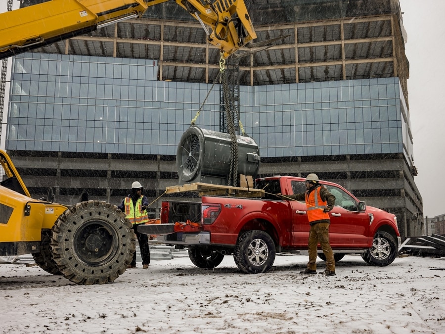 Workers standing behind a 2024 Ford F-150® pickup while a giant turbine motor is being lowered into the truck bed