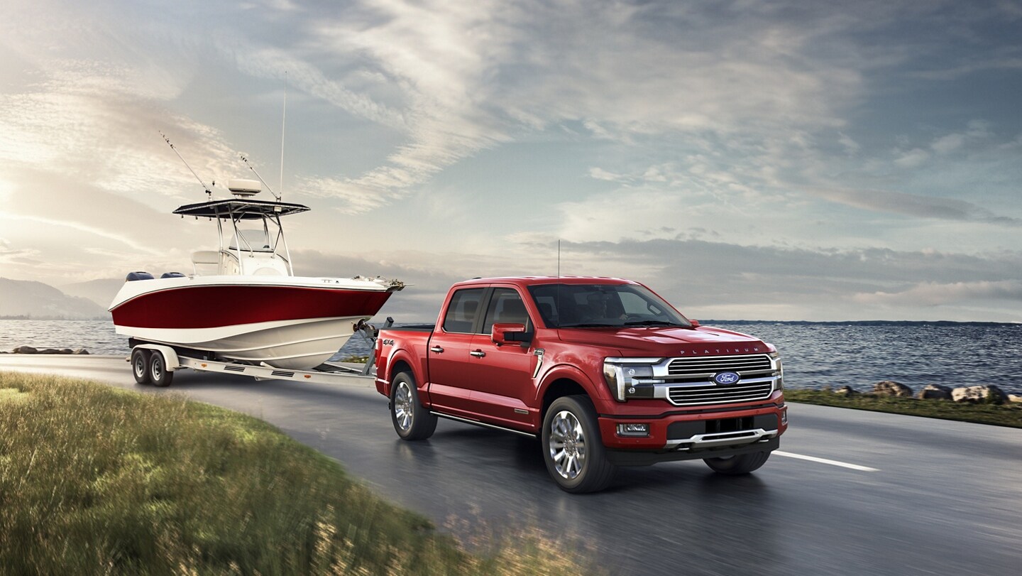 2024 Ford F-150® Platinum Plus pickup in Rapid Red pulling a boat near a lake