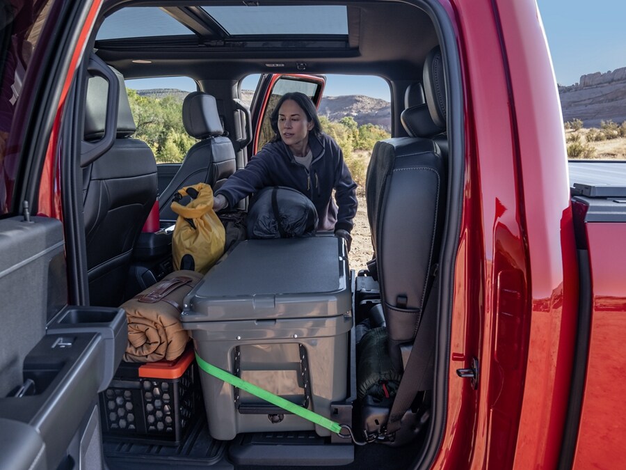 Woman loading items into the rear seating area of a 2024 Ford F-150® truck with the seats folded up
