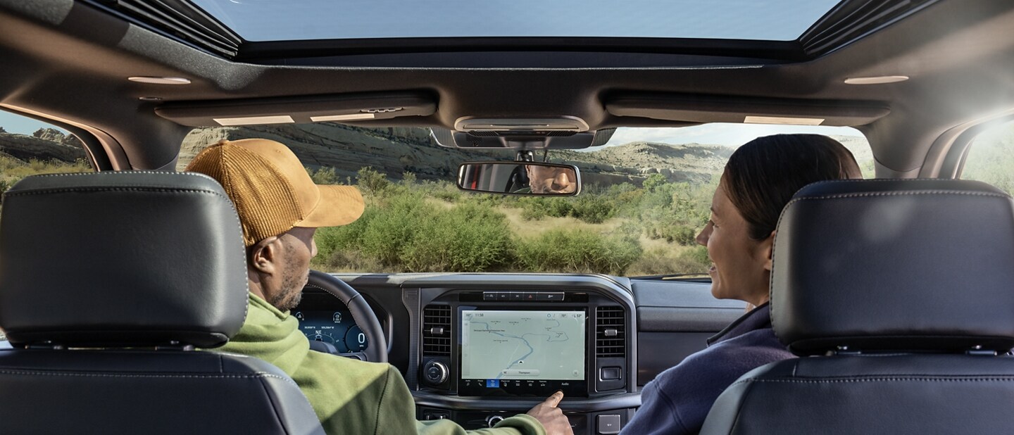 View from the back seat showing a man using the 12-inch touchscreen and a woman watching from the passenger seat
