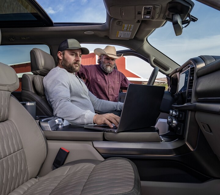 Interior of a 2024 Ford F-150® truck showing a man working on a laptop computer and another man looking in