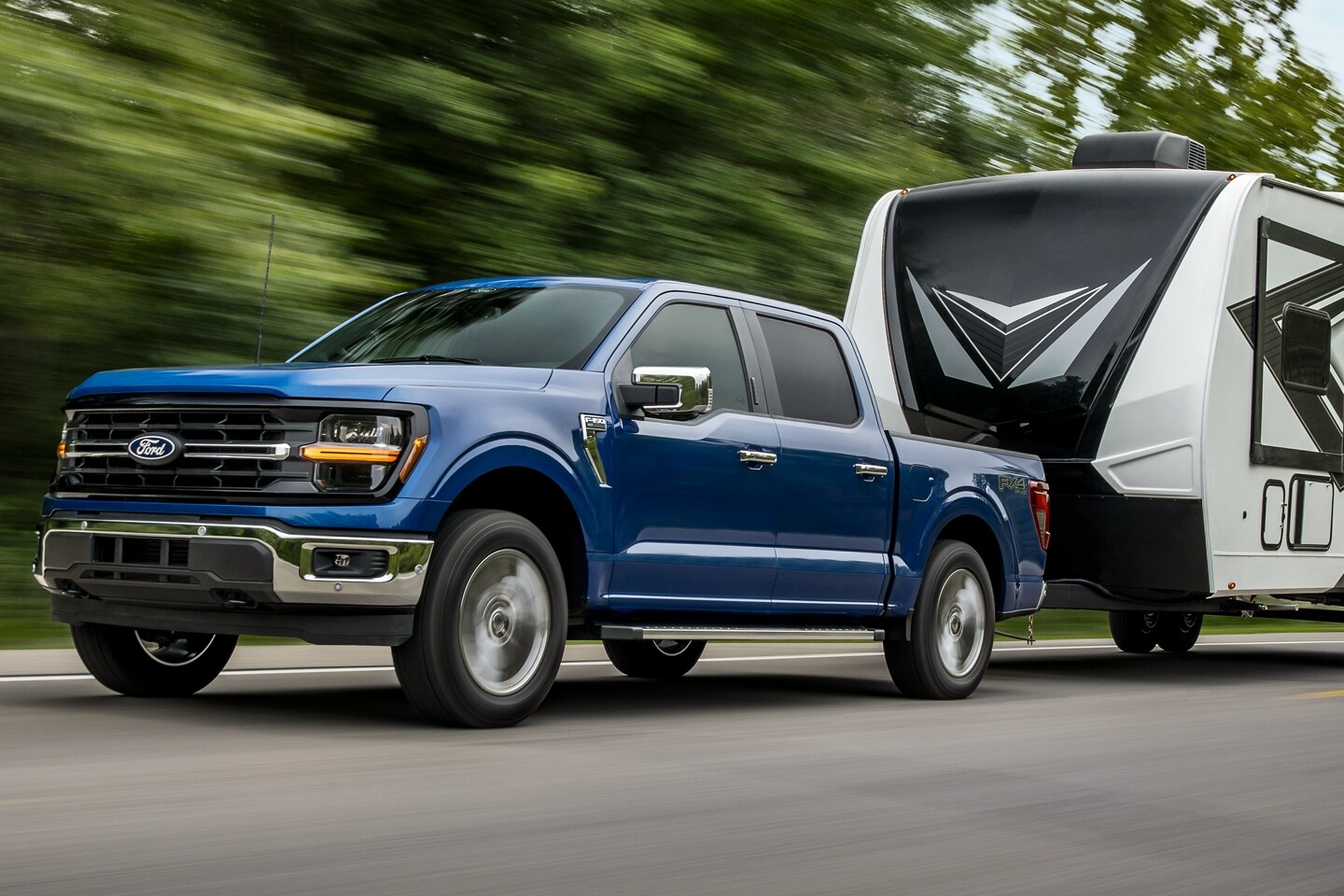  2024 Ford F-150 in Atlas Blue Metallic towing black and white trailer on highway. 