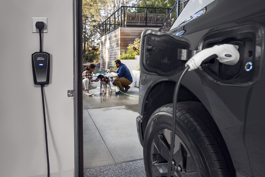 Charger connected to gray 2023 Ford F-150 Lightning® while a man and woman are washing their dog in the driveway