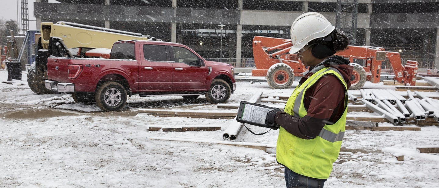Una persona en un sitio de construcción usando un tablet con una Ford F-150 Lightning® 2023 estacionada