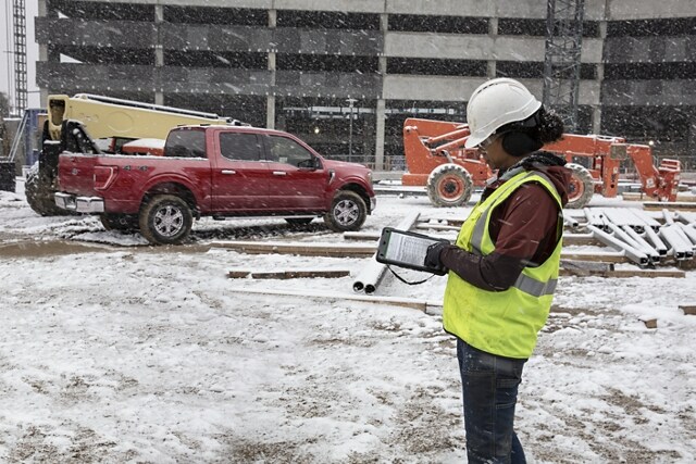 Person on construction site using a pad with a 2023 Ford F-150 Lightning® parked