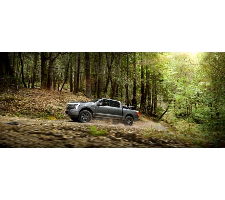 A 2023 Ford F-150 Lightning driving through a forest on a dirt road