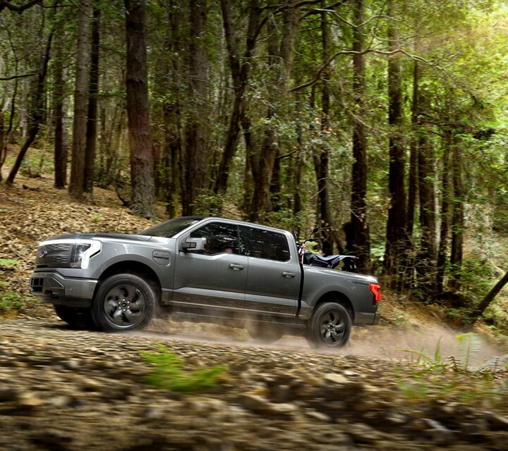 A 2023 Ford F-150 Lightning driving through a forest on a dirt road