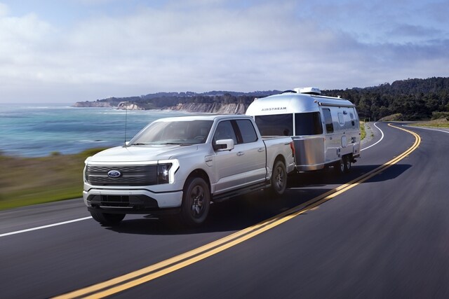 A 2023 Ford F-150 Lightning®  towing a camper on an oceanside road
