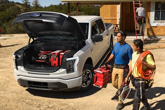 A 2023 Ford F-150 Lightning® at worksite with two people loading up the open frunk