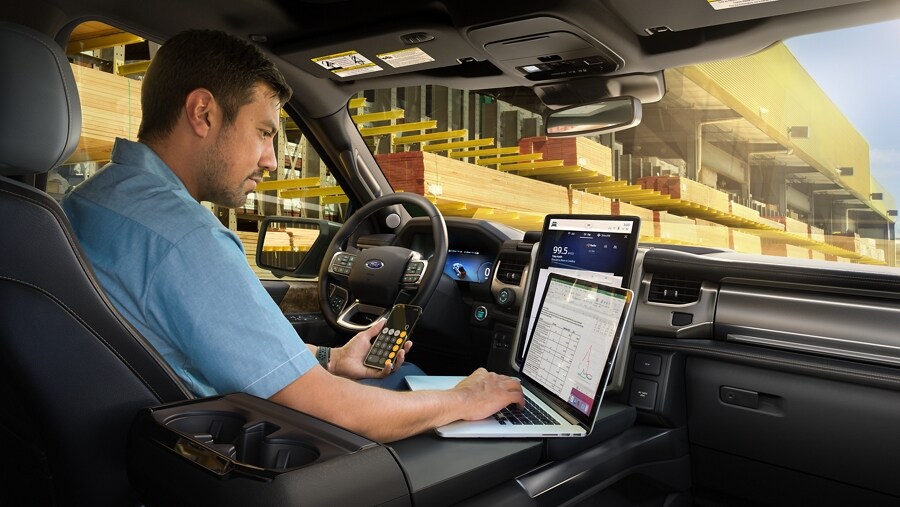 Interior of a parked 2023 Ford F-150 Lightning® with a man working on his computer on flat work surface