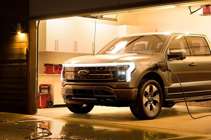 A 2023 Ford F-150 Lightning® powering a house as couple cleans branches off driveway