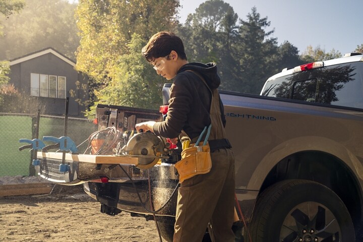 Guy cutting a board clamped on the tailgate of a 2023 Ford F-150 Lightning®