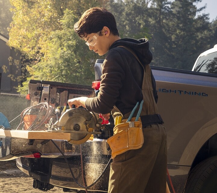 A guy sawing a board clamped to the tailgate of his 2023 Ford F-150 Lightning™