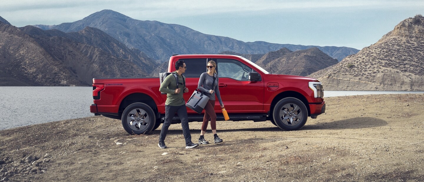 A 2023 Ford F-150 Lightning® parked at edge of mountain lake, mountains in background