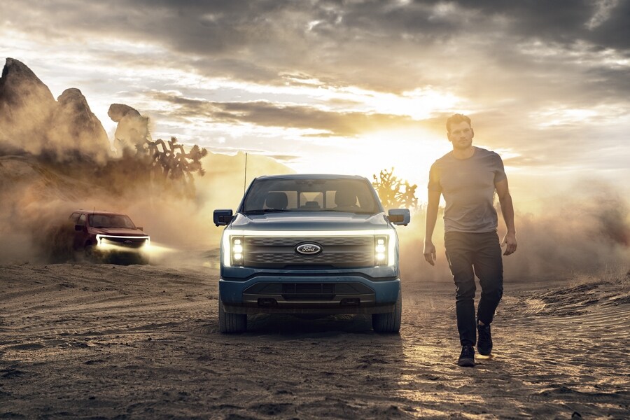 Lone guy walking through desert at dusk while two 2023 Ford F-150 Lightnings™ drive up behind him