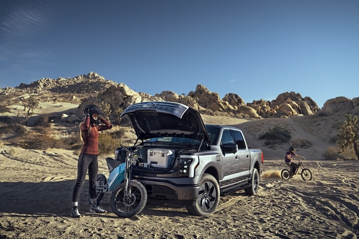 A 2023 F-150® Lightning® in rocky desert with frunk open as motorcyclists ride around it