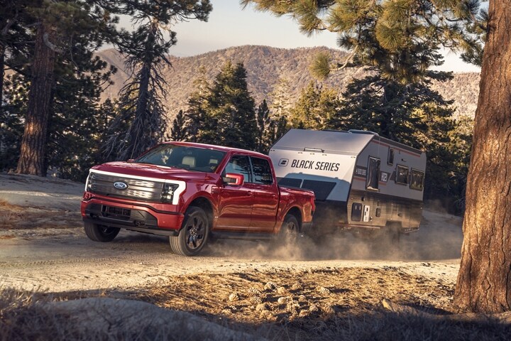 A 2023 Ford F-150 Lightning® towing a trailer through the woods