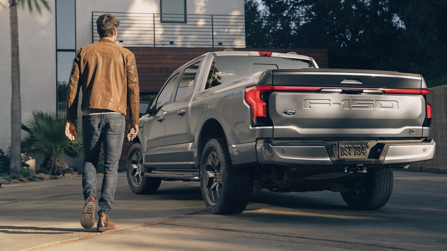 Rear shot of a 2023 Ford F-150 Lightning® in a driveway as a man walks toward it