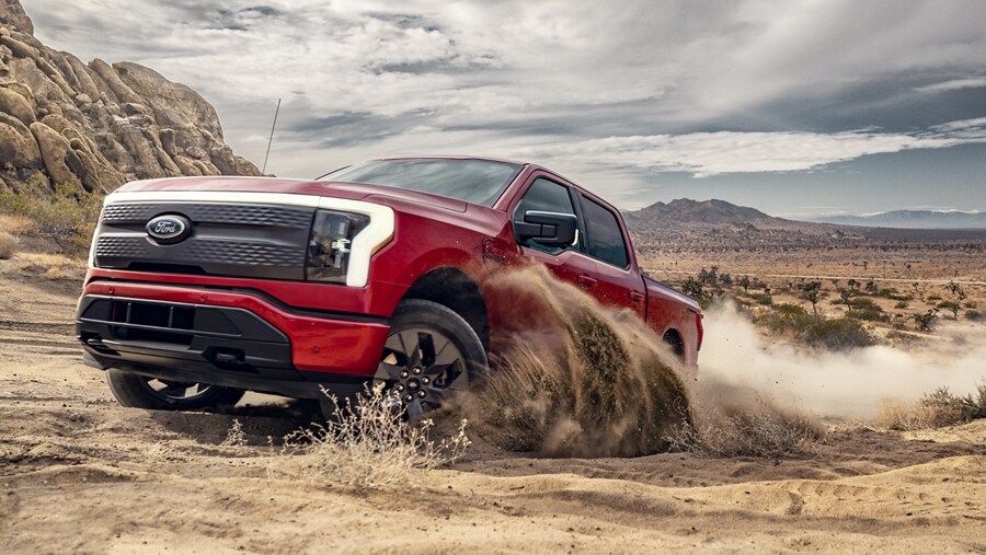 A 2023 Ford F-150 Lightning® being driven aggressively over desert trail, kicking up dust