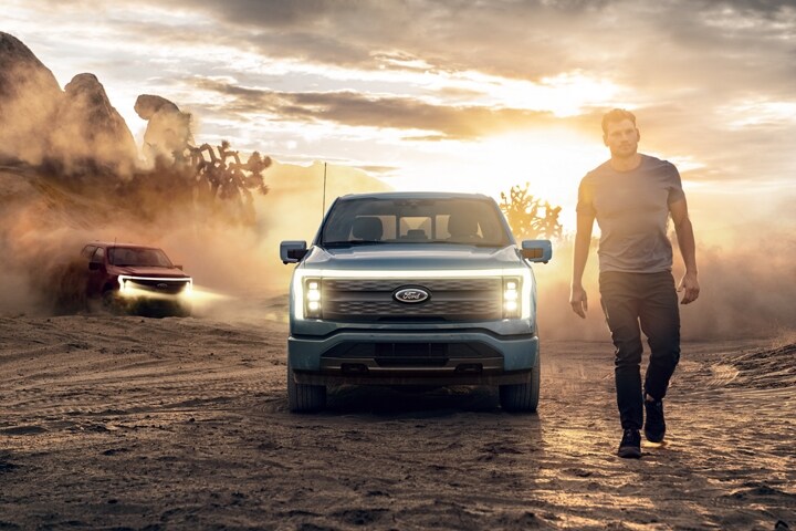 A man walks through desert at dusk, two 2023 Ford F-150 Lightnings® drive toward him