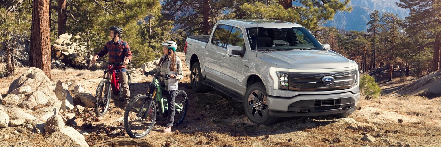 A couple on their bikes getting ready to ride the trails, alongside their silver Ford F-150 Lightning