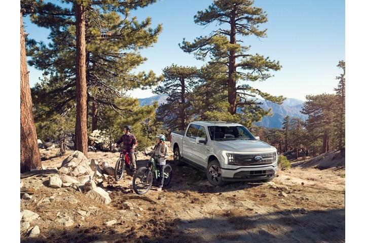 A 2023 Ford F-150 Lightning® in the woods as two mountain bikers prepare to hit trail