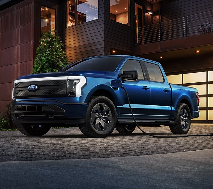 A 2023 Ford F-150 Lightning Platinum in driveway at home , plugged in to charger