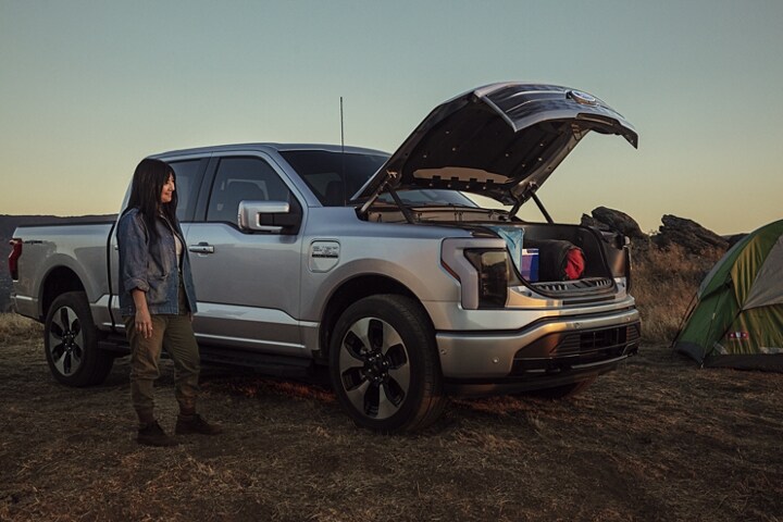 Una Ford F-150 Lightning® 2023 acampando con la Cajuela Delantera Mega Eléctrica​​​​​​​ abierta y una mujer parada junto a ella