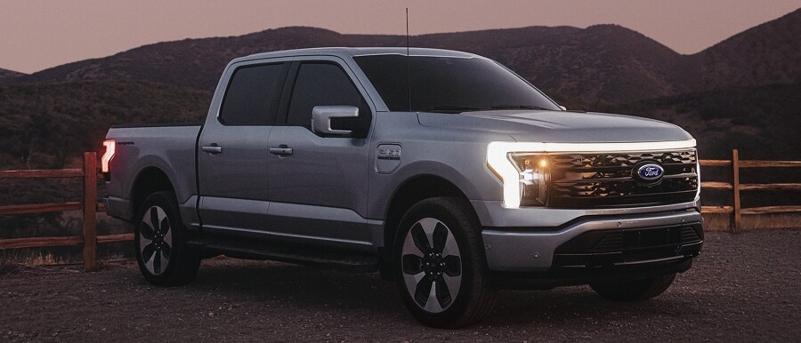 A 2023 Ford F-150 Lightning at dusk with its headlamps on