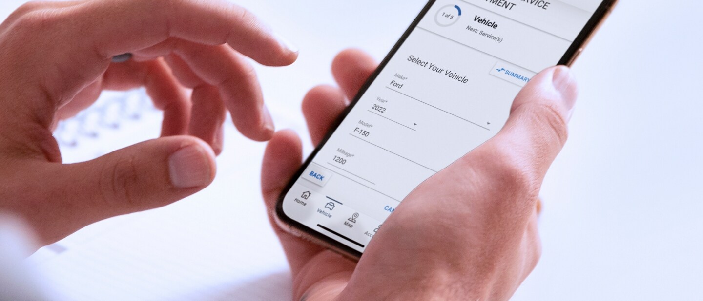 A hand holds a smartphone displaying the Schedule Service menu in the FordPass App
