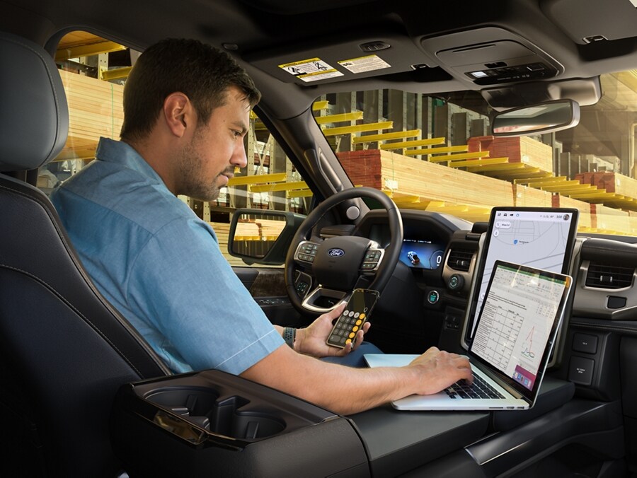 A man behind the wheel of a parked 2024 Ford F-150 Lightning® pickup truck. He is using the interior work surface as a desk