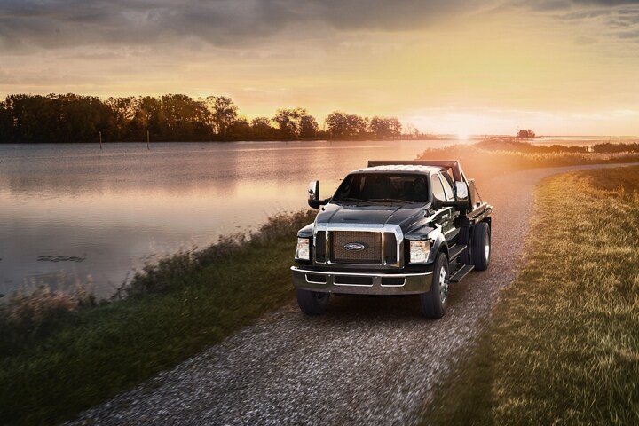 Ford F-750 Crew Cab 2024 en Agate Black con mejora de plataforma con estacas utilitarias andando por un camino de gravilla al atardecer