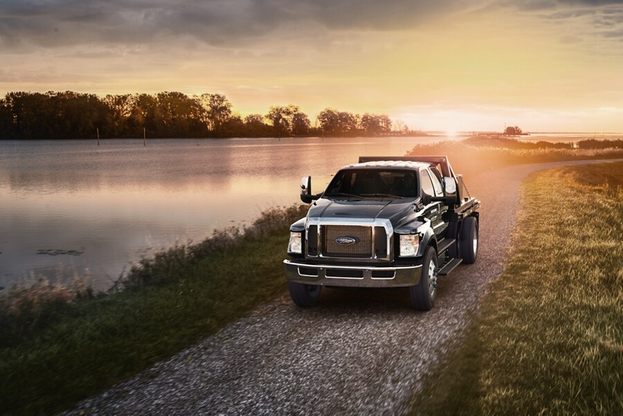 2024 Ford F-750 Crew Cab in Agate Black with utility stake bed upfit being driven near a lake