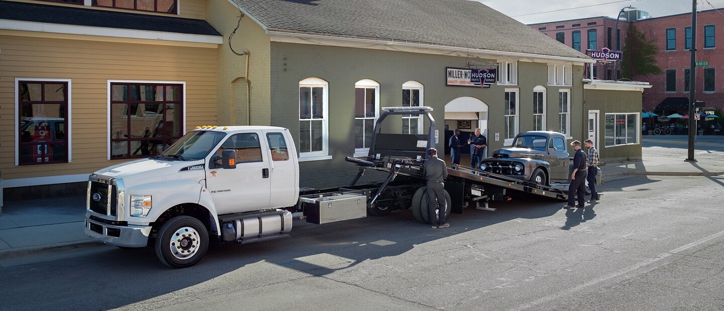 Car being loaded onto 2024 Ford F-650 SuperCab in Oxford White with rollback body flatbed and tow truck upfit