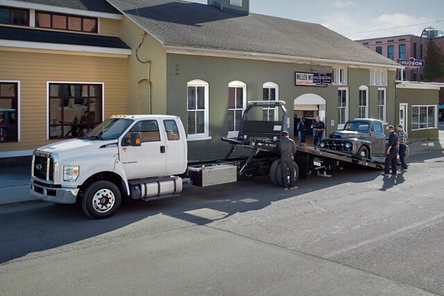 Car being loaded onto 2024 Ford F-650 SuperCab in Oxford White with rollback body flatbed and tow truck upfit
