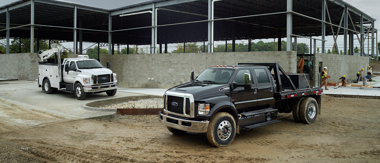 Ford F-750 SuperCab 2024 en Oxford White con mejora y Ford F-750 Crew Cab 2024 en Agate Black con mejora en un lugar de trabajo