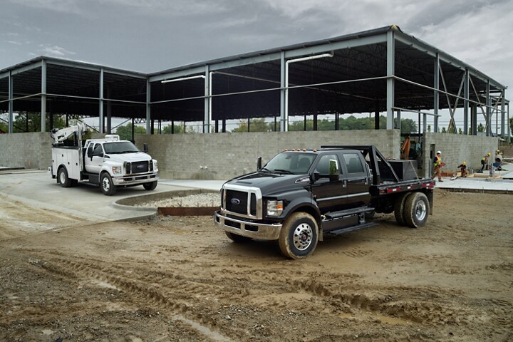 Ford F-750 SuperCab 2024 en Oxford White con mejora y Ford F-750 Crew Cab 2024 en Agate Black con mejora en un lugar de trabajo