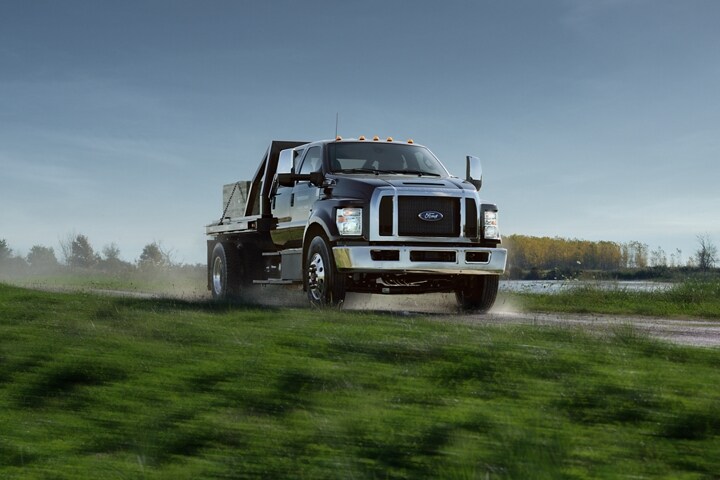 2024 Ford F-750 with utility stake bed upfit in Agate Black being driven on dirt road near grass and water