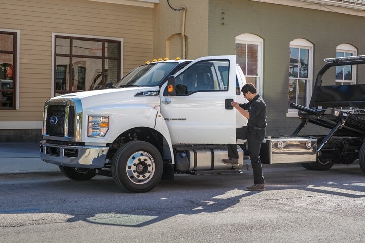 Una persona ingresando en una Ford F-650 SuperCab 2024 con plataforma para carrocería basculante y camioneta de remolque​​​​​​​ en Oxford White